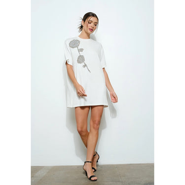 Woman wearing a white dress with floral design against a plain background