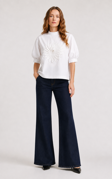 Woman wearing the Castca white floral appliqué top with dark wide-leg pants, front view.