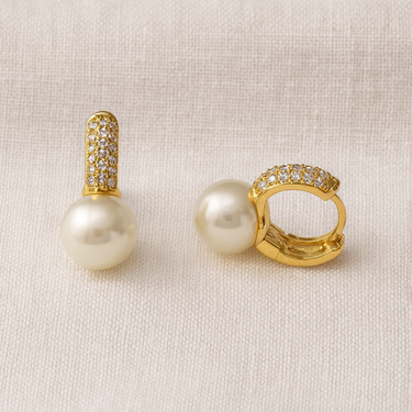 Clair Huggie Earrings, gold huggie hoop earrings with pavé-set surface and pearl drop detail, photographed on white linen background with soft editorial lighting.