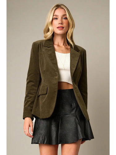 Model wearing the Cloe Corduroy Blazer Jacket in olive green featuring a tailored silhouette, notch lapels, single-button closure, flap pockets, and soft corduroy fabric, styled with a white crop top and black faux leather mini skirt.