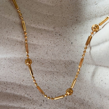 Colca Necklace by Matte, gold plated bar and bead chain with floral accents on ceramic surface