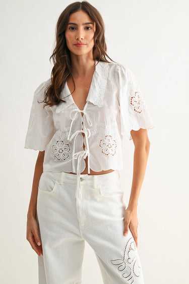 Woman wearing a white blouse with lace details on a plain background