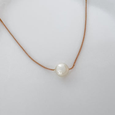 Close-up of Elara Necklace on gold chain with single pearl on white background