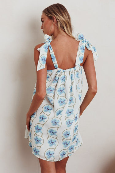Model in blue floral Ender Mini Dress showing lightweight cotton fabric and tie straps, back view.