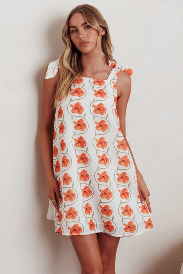 A woman wearing a floral mini dress with tied shoulder straps.