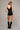 Black fitted bodysuit with metallic contour embroidery and deep V neckline, styled on a model in an editorial neutral setting, back view.