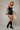 Black fitted bodysuit with metallic contour embroidery and deep V neckline, styled with a draped jacket on a model in an editorial neutral setting.