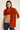 Woman wearing the Eto Pashmina in burnt orange chunky knit wool, cozy fall tones, warm light and natural background – Matte.