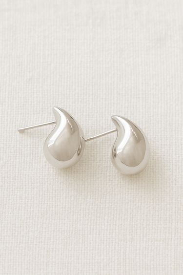 Felicia Stud Earrings in polished silver teardrop shape on beige linen background
