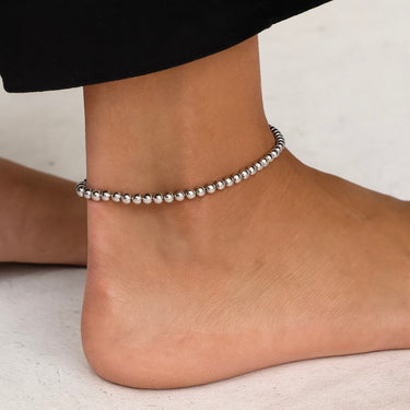 Silver beaded anklet on a foot against a neutral background