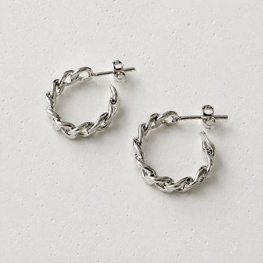 Genk Hoop Earrings featuring polished silver-plated hoop earrings with a braided chain-inspired texture, rounded hoop silhouette, mirror finish, secure hinged closure, lightweight design, and modern everyday style.