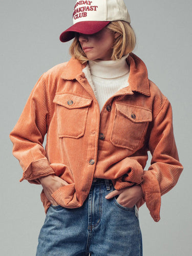 Front view of the Genova corduroy jacket styled open with a white mock-neck top, blue jeans, and a burgundy baseball cap, highlighting the oversized fit and flap chest pockets..