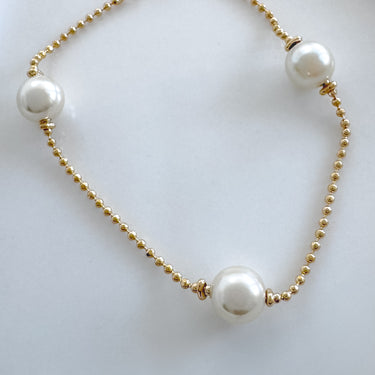 A gold-plated bracelet with white pearls and gold beads, displayed against a white background.