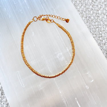 Gold disc bead bracelet with adjustable clasp on white textured surface.
