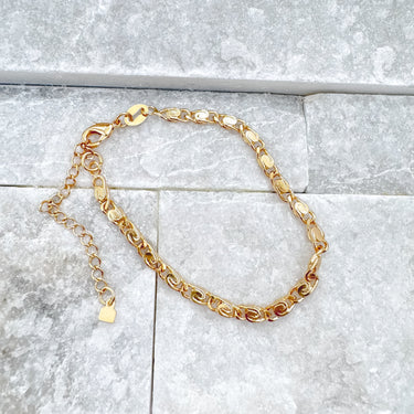 Gold chain link bracelet with polished oval links and adjustable clasp on gray stone background