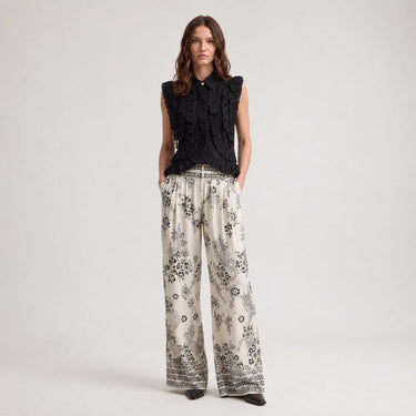 Woman wearing the black Harpenter ruffle blouse styled with printed wide-leg pants.