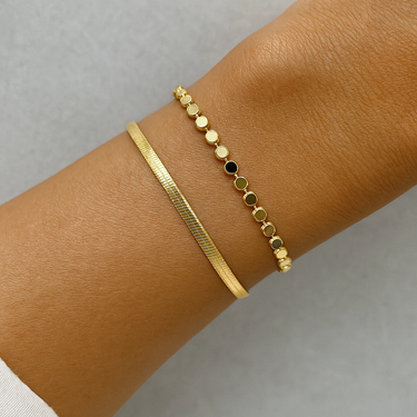 Gold double layered bracelet on a wrist against a neutral background.