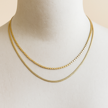 Gold double layered necklace on a mannequin with a plain background