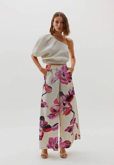 A model wearing floral print Hibiscus Pants with an elastic waistband and side pockets, paired with a beige spaghetti strap top.
