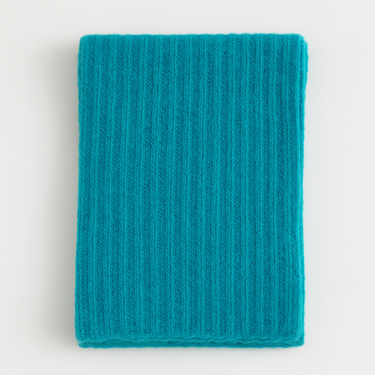 Hono Scarf in turquoise ribbed knit, soft textured scarf folded flat on beige background.