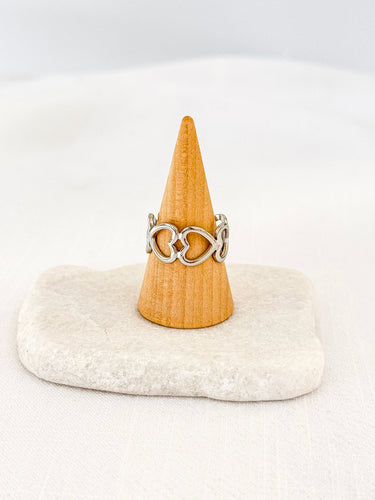 A gold-plated silver heart link ring displayed on a wooden stand with a white base.