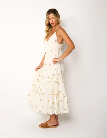 "side view of woman wearing ivory midi dress with gold star embroidery, v-neck, spaghetti straps, tiered skirt, tan sandals, summer resort style"