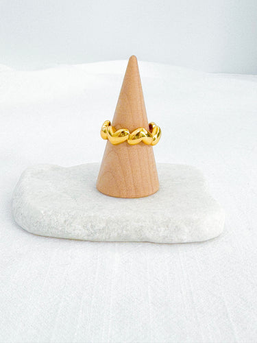 Gold-plated twisted heart sculptural ring displayed on wooden cone over marble base