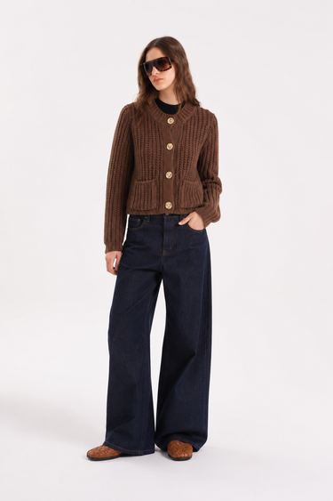 Woman wearing the Jutmy chunky knit cardigan in brown with gold-tone buttons, front patch pockets, and a relaxed cropped fit.