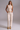 Woman wearing a beige top and brown pants with a belt against a gray background