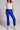 Model wearing cobalt blue slim pants with coated finish and white top — modern city look.
