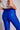 Model wearing cobalt blue slim pants with coated finish and white top — modern city look close up back view.