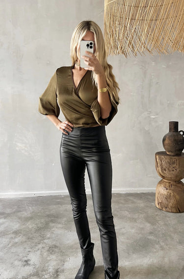 Model wearing Kuta Skinny black foil stretch pants with high waist and ankle fit.
