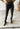 A person wearing black skinny pants and black boots standing in front of a mirror.