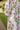 Woman wearing Lissandra Maxi Dress with pink and green floral print walking outdoors in garden setting.