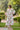 Woman wearing Lissandra Maxi Dress with pink and green floral print walking outdoors in garden setting.