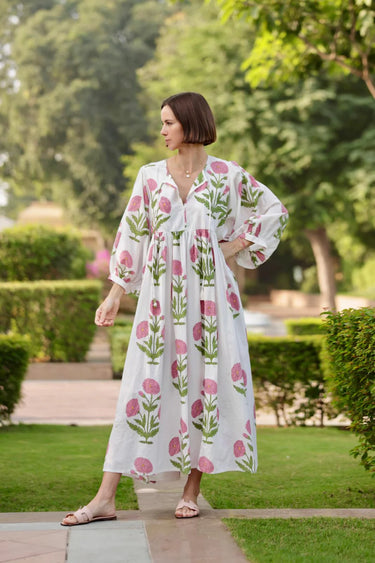 Woman wearing Lissandra Maxi Dress with pink and green floral print walking outdoors in garden setting.