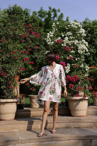 Model wearing white mini dress with pink floral print and long sleeves, resort style.