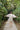 A person wearing a white mini dress with a floral pattern, walking away from the camera on a path surrounded by greenery.