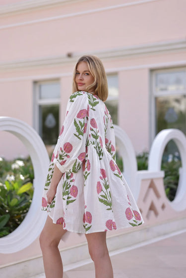 Model wearing white mini dress with pink floral print and long sleeves, resort style.