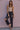 Woman wearing a beige tank top and black distressed jeans against a pink wall.