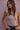 Woman wearing a beige tank top against a pink wall