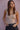 Woman wearing a beige tank top against a pink wall