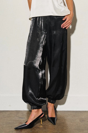 Woman wearing Lumit black balloon pants featuring a relaxed silhouette, elastic waistband, gathered ankle hem, and a lustrous finish.