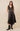 A woman wearing a black satin sleeveless dress with a V-neckline, lace trim, and stud embellishments. The dress has a flowy silhouette and an asymmetrical hem.