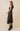 Model wearing Maira Asymmetrical Dress in black satin, showing sleeveless fit and asymmetrical hem.