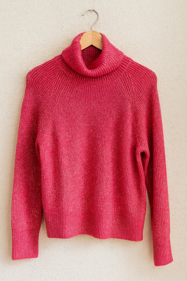 Pink turtleneck sweater on a wooden hanger against a beige wall
