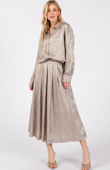 Model wearing the Maui Blouse in champagne — metallic fabric, relaxed fit, long sleeves, button-down front, paired with matching skirt, elegant shimmer look.