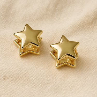 Gold star-shaped huggie earrings on white linen backdrop, Melfy Huggie Earrings.