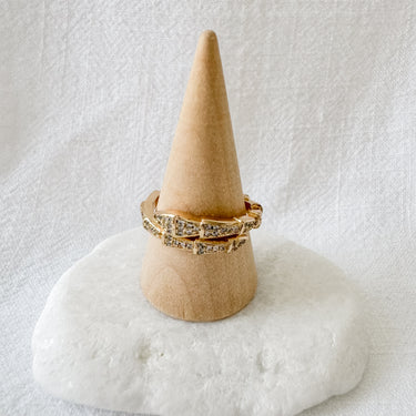A gold-filled pave ring with a snake design displayed on a beige cone-shaped stand against a white background.