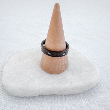 A gold-plated band ring displayed on a white cushion atop a wooden stand, with a simple and sleek design.